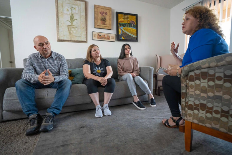 Global Refuge employee completing an intake for a family. Couple and teenage daughter talking with an Global Refuge employee in a living room.